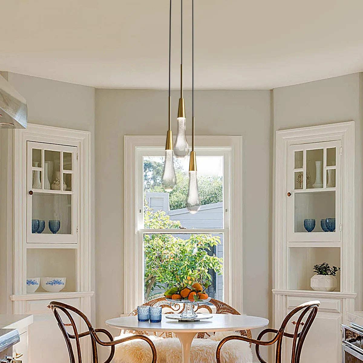 A pendant light with black PVC cords and brass-finished integrated LED lights, hanging over a dining table in a room with light-colored walls.