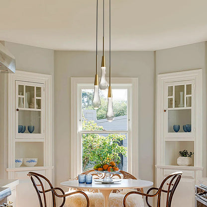 A pendant light with black PVC cords and brass-finished integrated LED lights, hanging over a dining table in a room with light-colored walls.